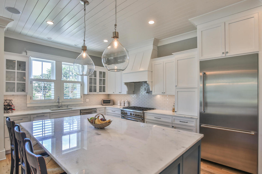 Design ideas for a beach style l-shaped kitchen in Charleston with an undermount sink, shaker cabinets, white cabinets, white splashback, subway tile splashback, stainless steel appliances, medium hardwood floors, with island and brown floor.