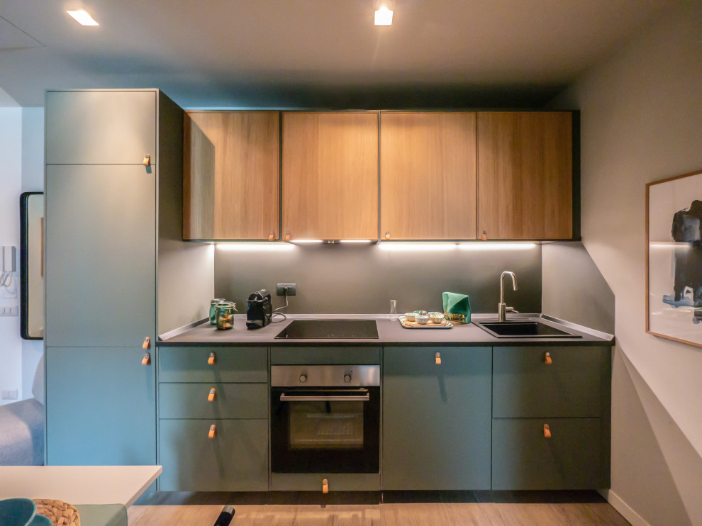 This is an example of a small contemporary single-wall open plan kitchen in Milan with a single-bowl sink, flat-panel cabinets, green cabinets, laminate benchtops, grey splashback, stainless steel appliances, porcelain floors, no island, beige floor and grey benchtop.