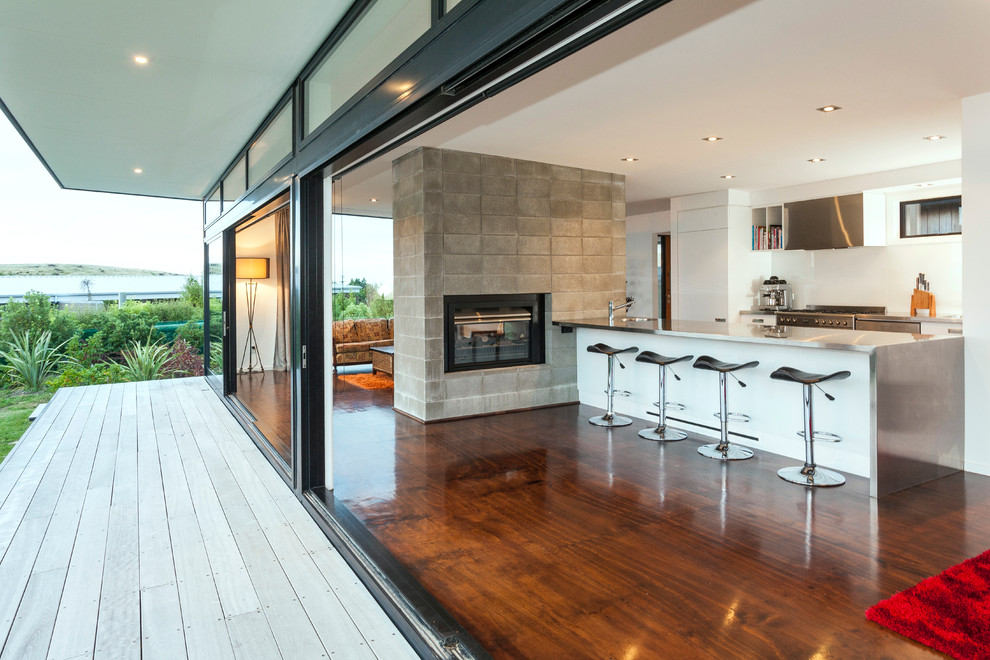 Inspiration for a mid-sized contemporary kitchen in Christchurch with stainless steel benchtops, white splashback, glass sheet splashback, stainless steel appliances and plywood floors.