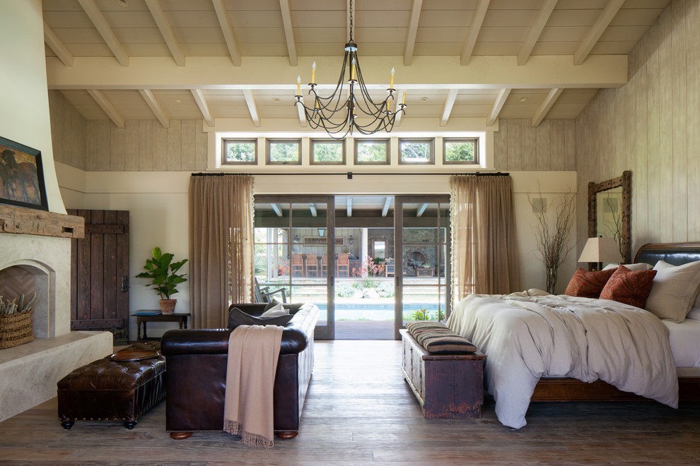 Photo of a country master bedroom in San Diego with beige walls, a standard fireplace, dark hardwood floors and brown floor.
