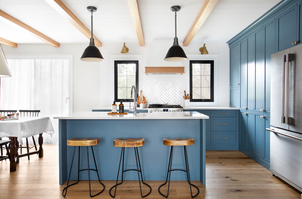 Inspiration for a mid-sized country eat-in kitchen in Montreal with shaker cabinets, blue cabinets, quartz benchtops, white splashback, stainless steel appliances, with island, white benchtop and medium hardwood floors.