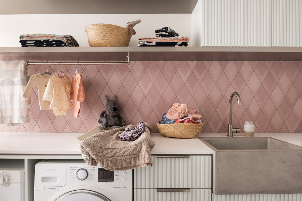 Design ideas for a mid-sized contemporary single-wall utility room in Perth with a farmhouse sink, quartz benchtops, pink splashback, ceramic splashback, a side-by-side washer and dryer and white benchtop.