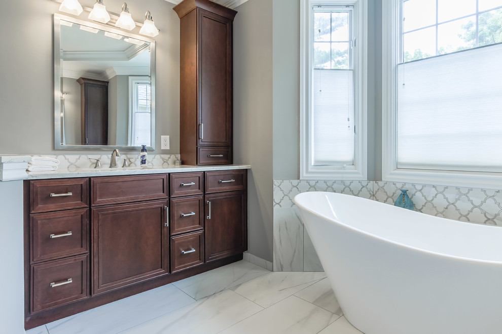 Photo of a large transitional master bathroom in Detroit with recessed-panel cabinets, dark wood cabinets, a freestanding tub, a corner shower, white tile, marble, white walls, marble floors, an undermount sink, engineered quartz benchtops, white floor, a hinged shower door and white benchtops.