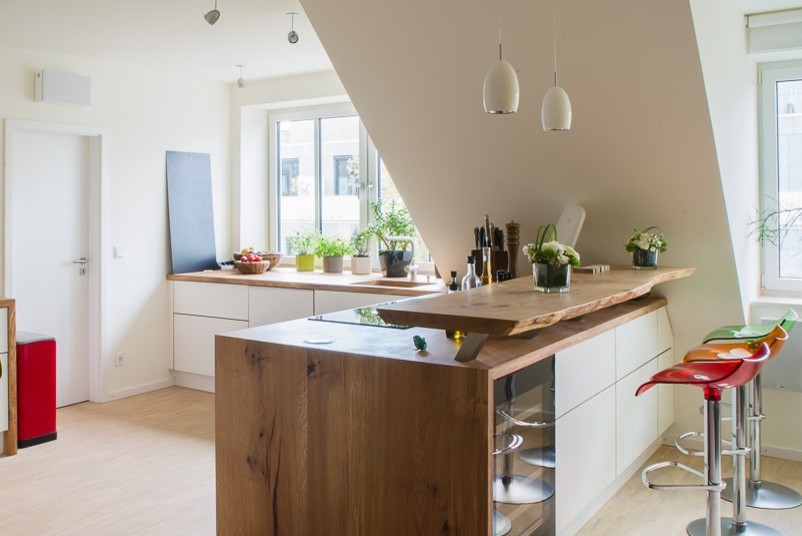 Große, Offene Moderne Küche in L-Form mit flächenbündigen Schrankfronten, weißen Schränken, Arbeitsplatte aus Holz, Küchenrückwand in Weiß, Halbinsel, integriertem Waschbecken, Küchengeräten aus Edelstahl, hellem Holzboden und braunem Boden in Hannover