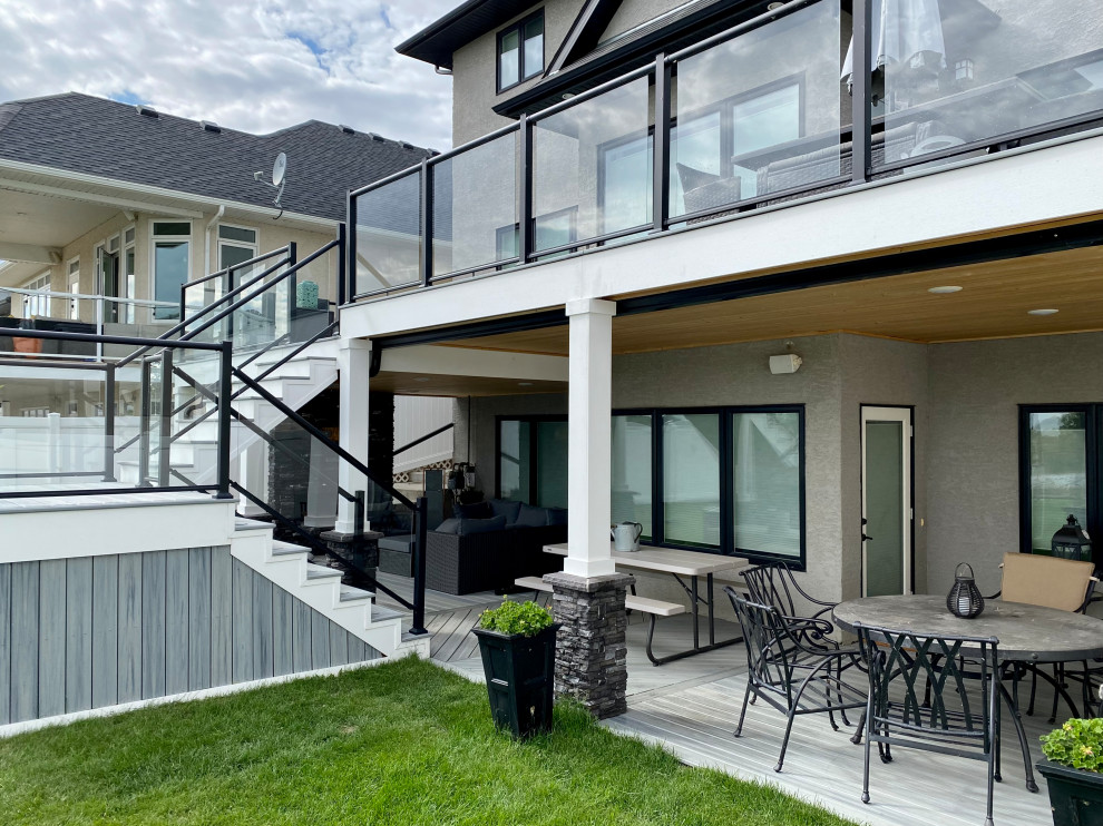 This is an example of a large modern backyard and first floor deck in Other with with fireplace, a roof extension and glass railing.