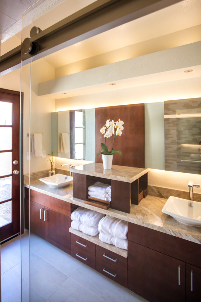 Inspiration for a small transitional bathroom in Phoenix with flat-panel cabinets, medium wood cabinets, an alcove tub, a shower/bathtub combo, a one-piece toilet, beige tile, porcelain tile, beige walls, porcelain floors, a vessel sink, granite benchtops, beige floor and a sliding shower screen.