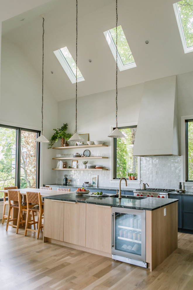 Design ideas for a modern l-shaped kitchen in Raleigh with a single-bowl sink, shaker cabinets, blue cabinets, granite benchtops, white splashback, ceramic splashback, stainless steel appliances, light hardwood floors, with island, yellow floor, black benchtop and vaulted.