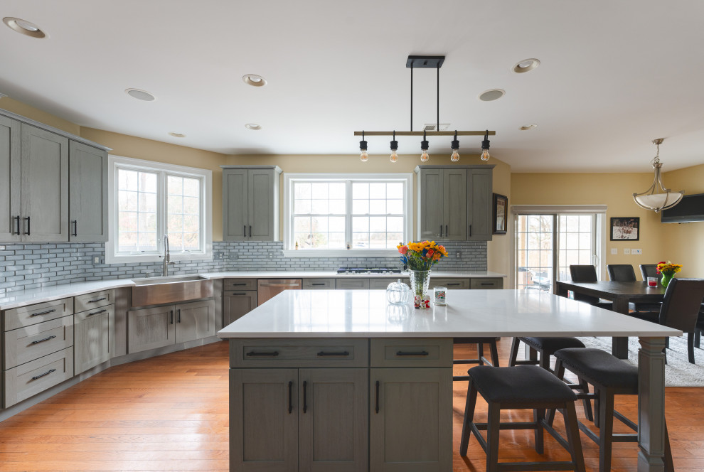 Inspiration for a large transitional u-shaped medium tone wood floor and brown floor eat-in kitchen remodel with a farmhouse sink, shaker cabinets, gray cabinets, quartz countertops, gray backsplash, glass tile backsplash, stainless steel appliances, an island and white countertops