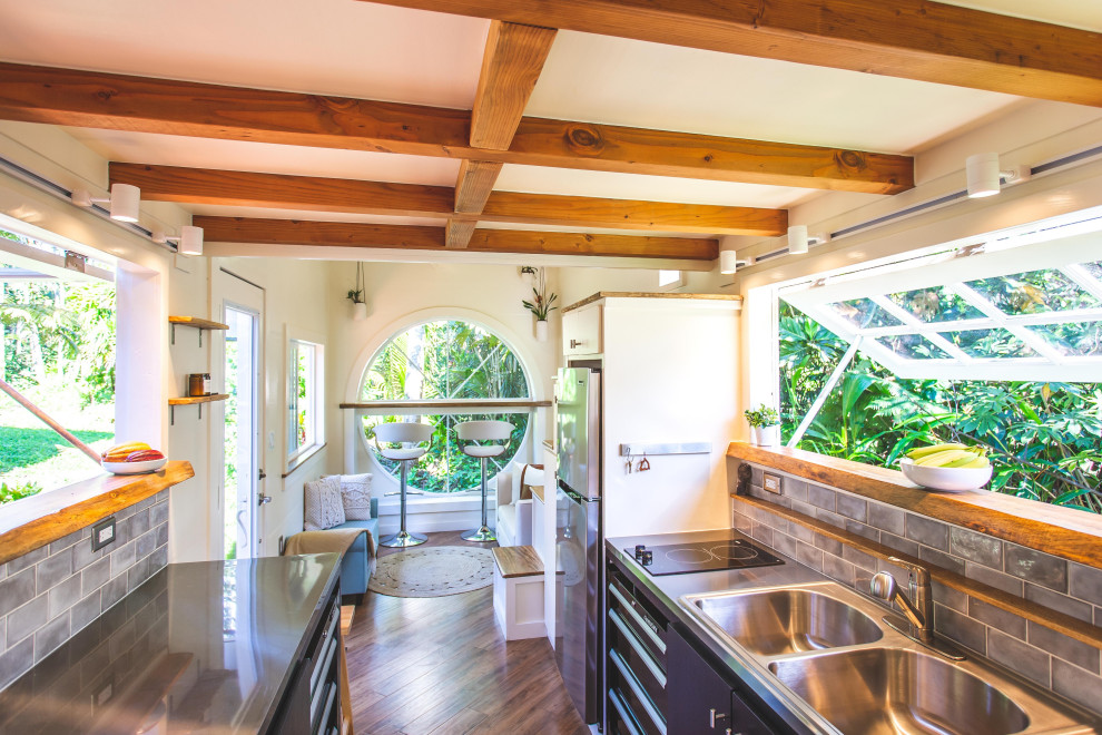 Photo of a small beach style u-shaped eat-in kitchen in Hawaii with a double-bowl sink, flat-panel cabinets, black cabinets, stainless steel benchtops, grey splashback, ceramic splashback, stainless steel appliances, laminate floors, with island, grey benchtop and exposed beam.