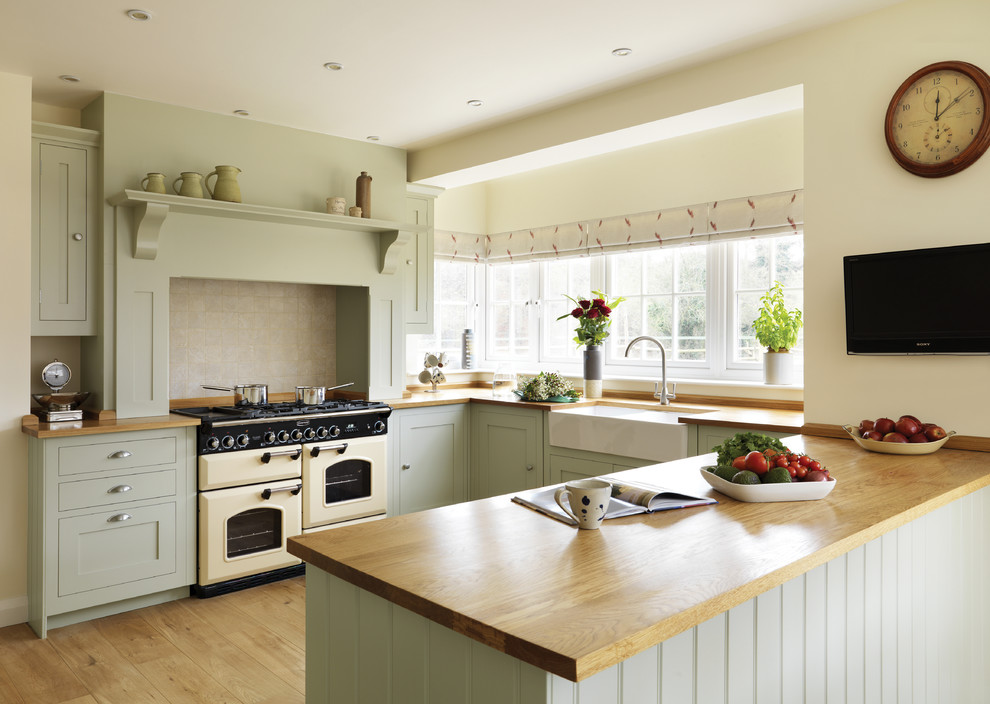 Inspiration for a traditional u-shaped kitchen in London with a farmhouse sink, green cabinets and a peninsula.