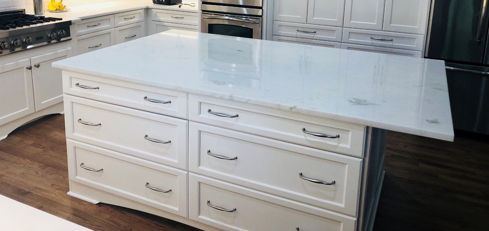 This is an example of a classic kitchen with a single-bowl sink, raised-panel cabinets, white cabinets, quartz worktops, white splashback, ceramic splashback, medium hardwood flooring, an island and white worktops.