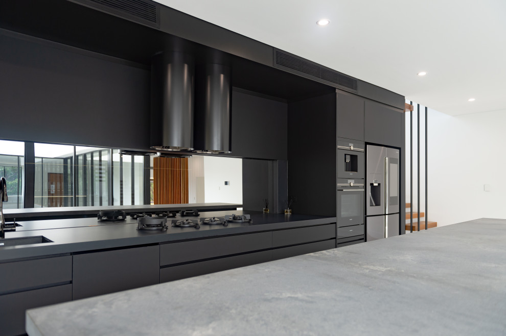 Exemple d'une grande cuisine parallèle industrielle avec des portes de placard noires, un plan de travail en quartz modifié, une crédence miroir, îlot et un plan de travail gris.
