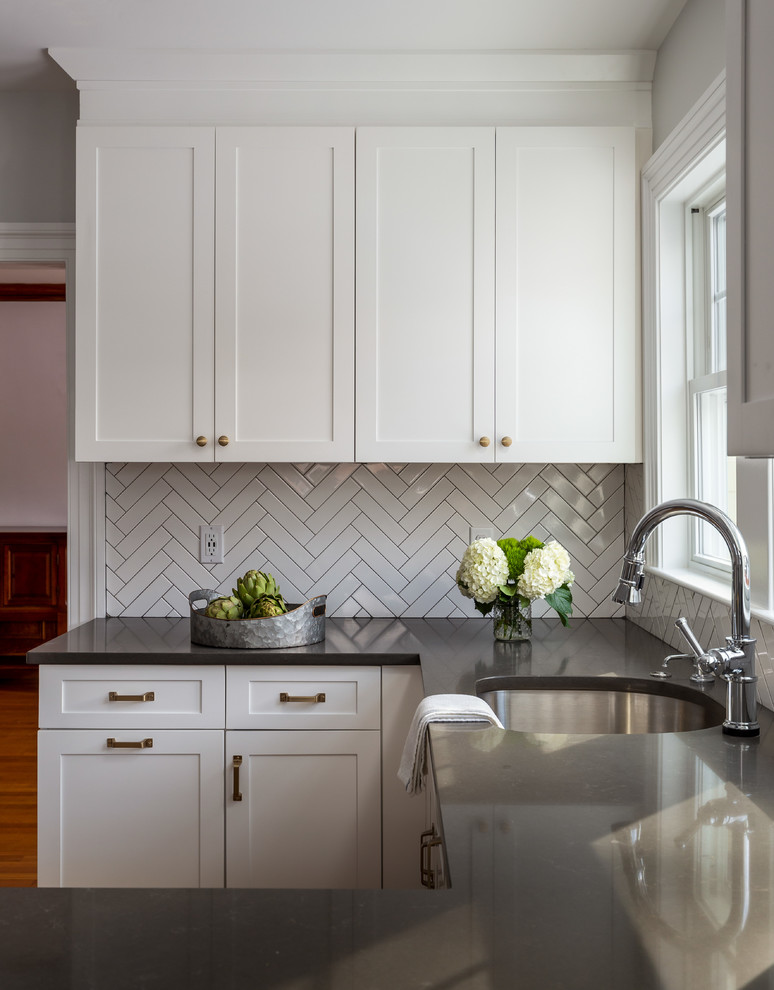 Example of a mid-sized transitional u-shaped light wood floor and brown floor enclosed kitchen design in Boston with an undermount sink, shaker cabinets, white cabinets, quartz countertops, gray backsplash, ceramic backsplash, stainless steel appliances, a peninsula and gray countertops