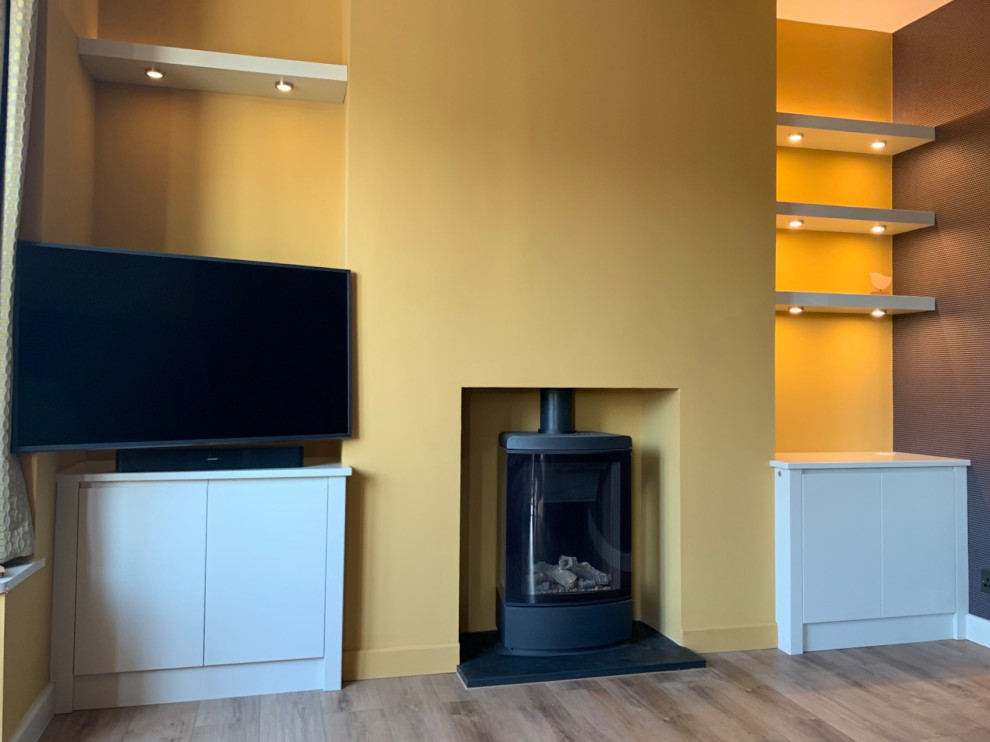 Imagen de salón contemporáneo pequeño con paredes amarillas, suelo de madera oscura, estufa de leña y televisor colgado en la pared