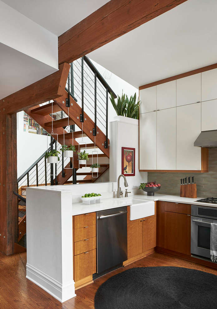 Eclectic kitchen in Chicago with a farmhouse sink, flat-panel cabinets, medium wood cabinets, grey splashback, stainless steel appliances, medium hardwood floors, a peninsula, brown floor and white benchtop.