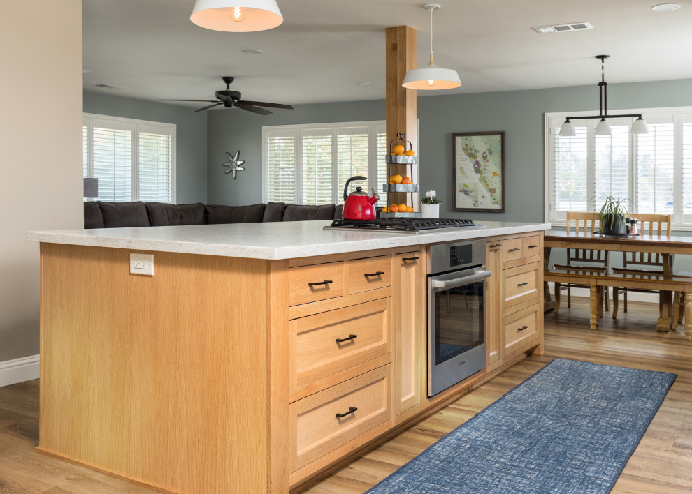 Photo of a mid-sized contemporary open plan kitchen in Other with a farmhouse sink, shaker cabinets, light wood cabinets, quartz benchtops, stainless steel appliances, vinyl floors, multiple islands, brown floor and grey benchtop.