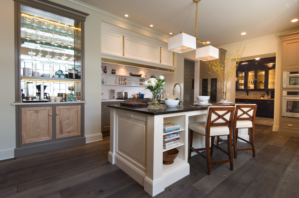 This is an example of a large traditional galley open plan kitchen in Chicago with an undermount sink, recessed-panel cabinets, white cabinets, onyx benchtops, white splashback, stone slab splashback, stainless steel appliances, medium hardwood floors, with island and brown floor.