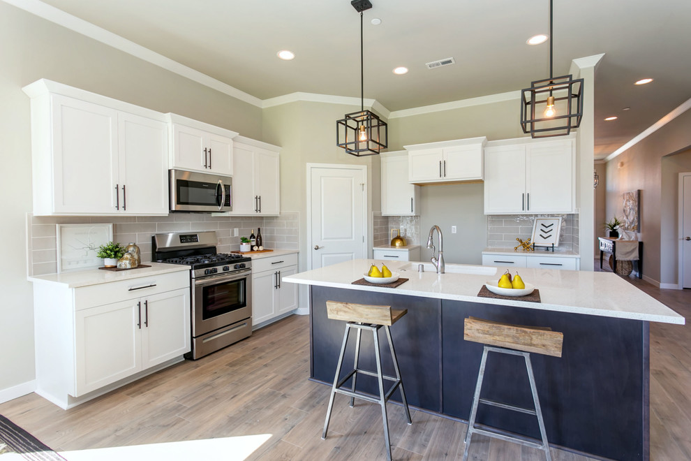Mid-sized transitional l-shaped laminate floor open concept kitchen photo in Seattle with an undermount sink, shaker cabinets, white cabinets, quartz countertops, gray backsplash, subway tile backsplash, stainless steel appliances, an island and white countertops