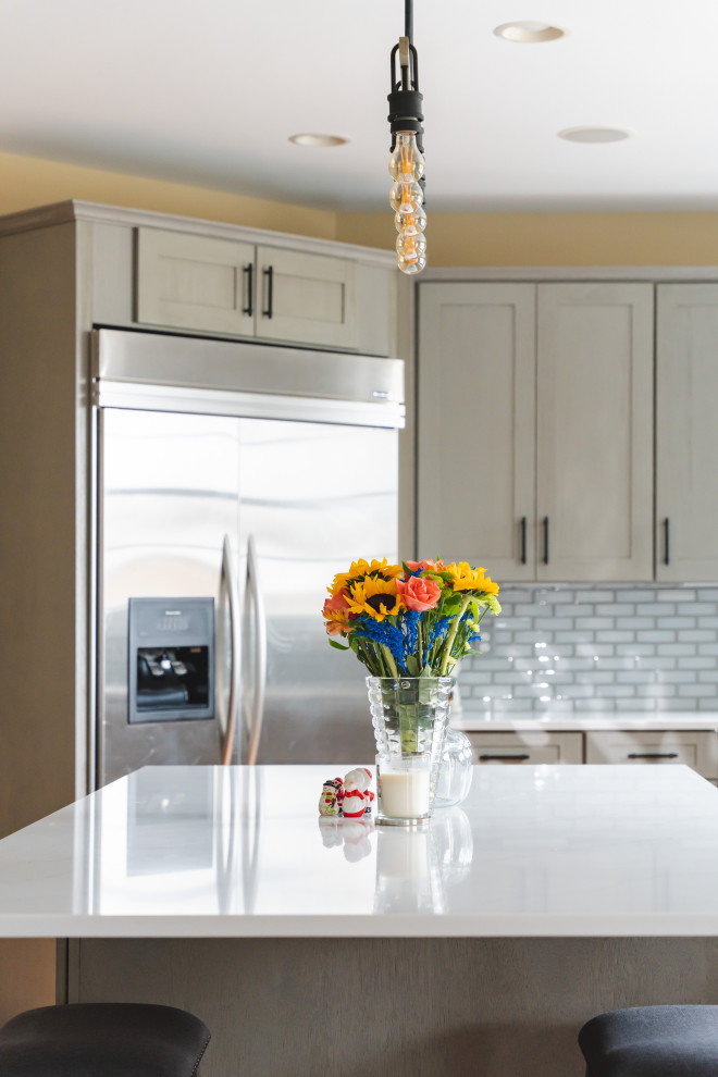 Large transitional u-shaped medium tone wood floor and brown floor eat-in kitchen photo with a farmhouse sink, shaker cabinets, gray cabinets, quartz countertops, gray backsplash, glass tile backsplash, stainless steel appliances, an island and white countertops