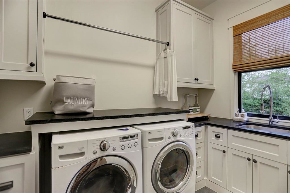 Mid-sized transitional l-shaped utility room in Houston with an undermount sink, shaker cabinets, white cabinets, granite benchtops, white walls, travertine floors, a side-by-side washer and dryer, grey floor and black benchtop.