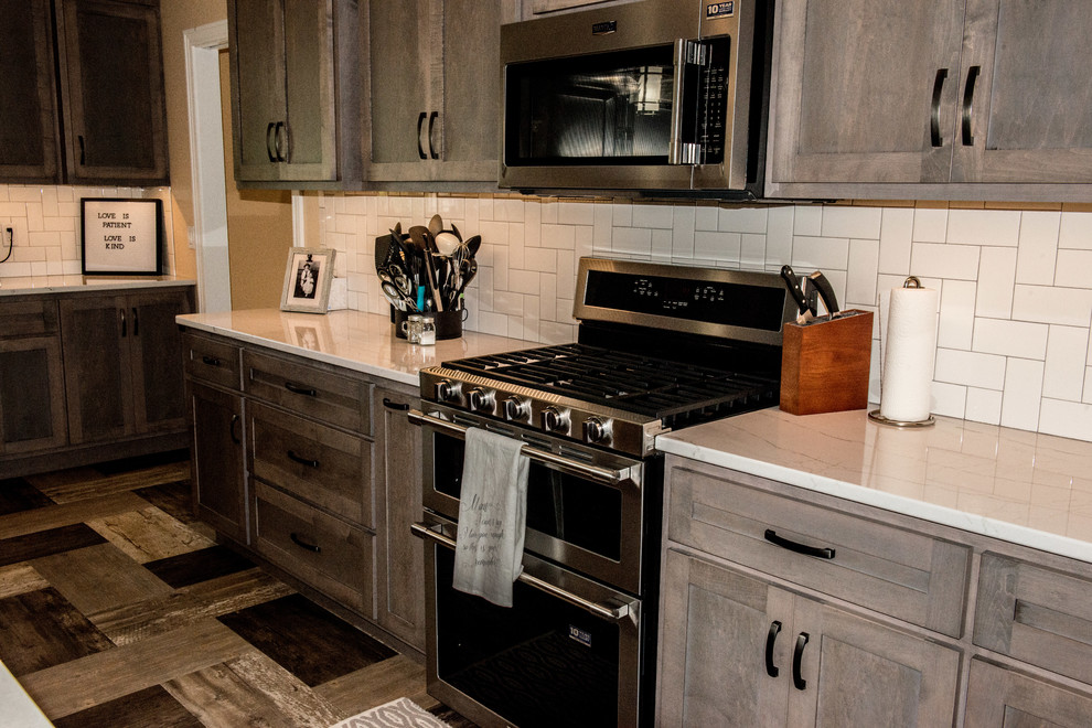 Open concept kitchen - large transitional l-shaped vinyl floor and multicolored floor open concept kitchen idea with a farmhouse sink, shaker cabinets, gray cabinets, quartz countertops, white backsplash, subway tile backsplash, stainless steel appliances, an island and white countertops