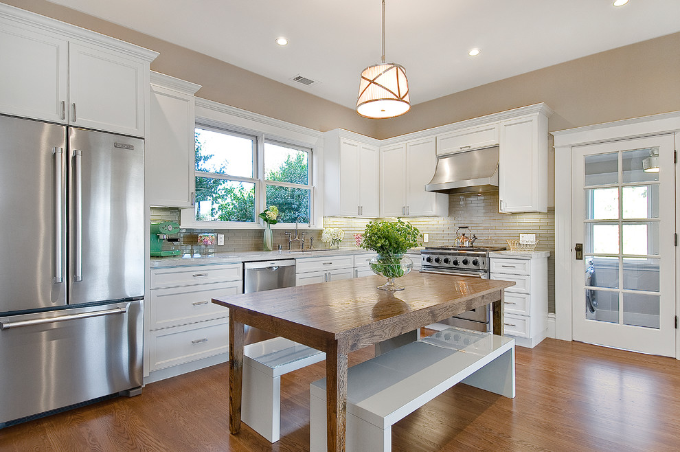 Design ideas for a mid-sized modern l-shaped eat-in kitchen in San Francisco with white cabinets, stainless steel appliances, an undermount sink, recessed-panel cabinets, marble benchtops, beige splashback, ceramic splashback, medium hardwood floors, with island and brown floor.