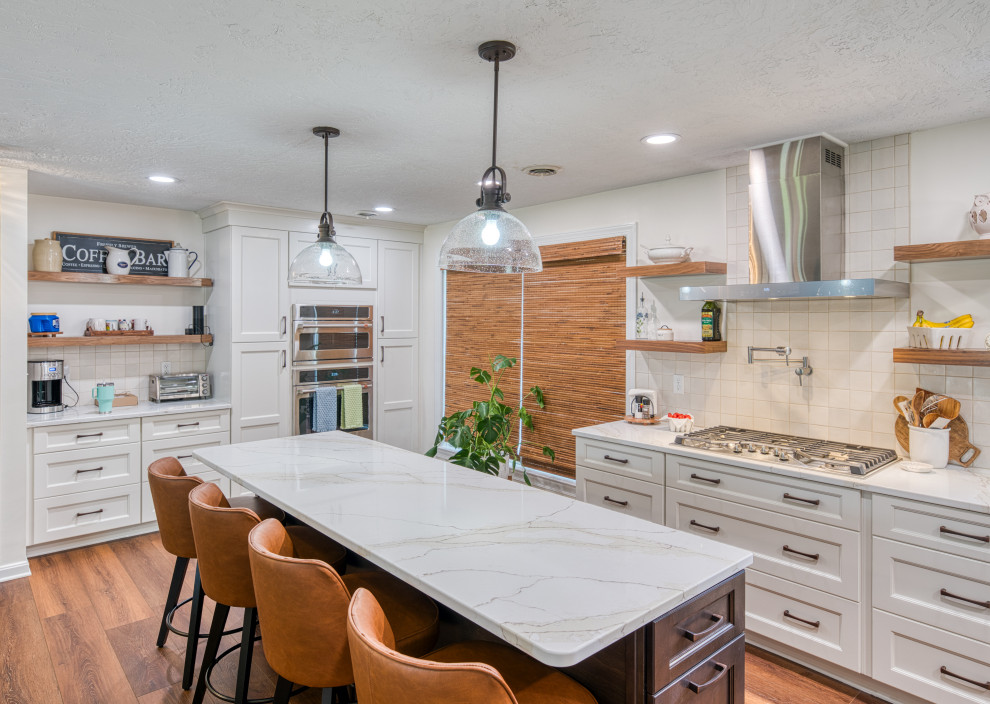 Kitchen - transitional l-shaped medium tone wood floor and brown floor kitchen idea with recessed-panel cabinets, white cabinets, white backsplash, stainless steel appliances, an island and white countertops