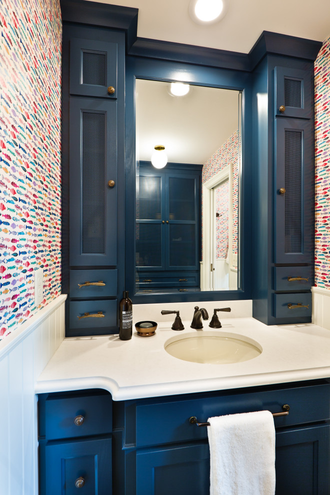Design ideas for a mid-sized traditional kids bathroom in Minneapolis with flat-panel cabinets, blue cabinets, an alcove tub, a shower/bathtub combo, a one-piece toilet, white tile, ceramic tile, multi-coloured walls, porcelain floors, an undermount sink, engineered quartz benchtops, brown floor, a shower curtain, white benchtops, an enclosed toilet, a single vanity, a built-in vanity and wallpaper.