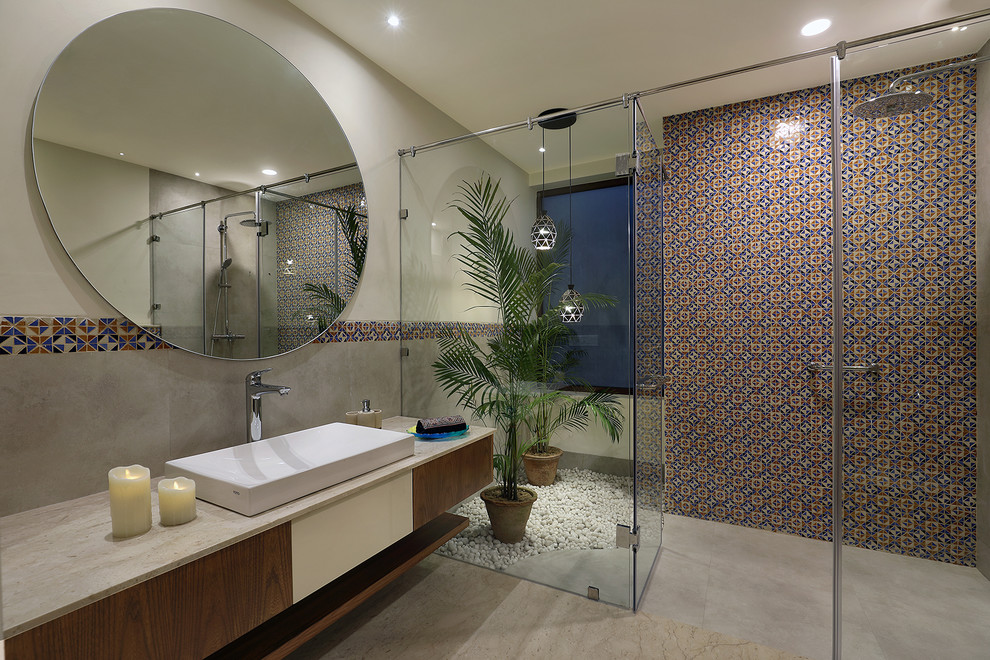 This is an example of a contemporary bathroom in Delhi with flat-panel cabinets, medium wood cabinets, a curbless shower, multi-coloured tile, grey walls, a vessel sink, grey floor, a hinged shower door and beige benchtops.