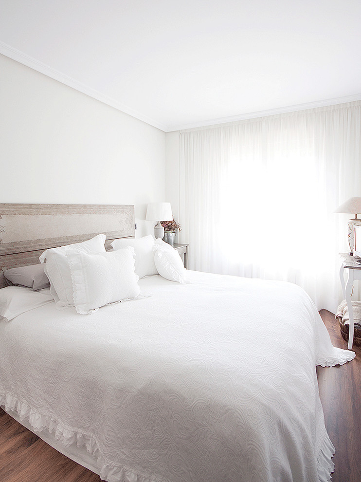 Design ideas for a large traditional master bedroom in Madrid with white walls, medium hardwood floors and no fireplace.
