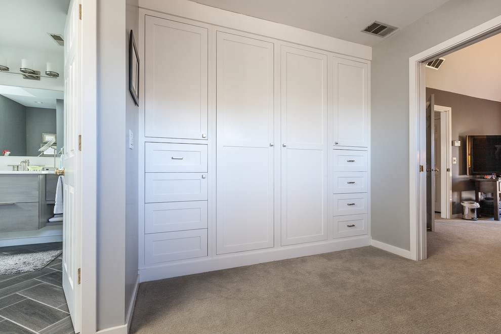 This is an example of a large modern men's built-in wardrobe in Chicago with shaker cabinets, white cabinets, carpet and beige floor.