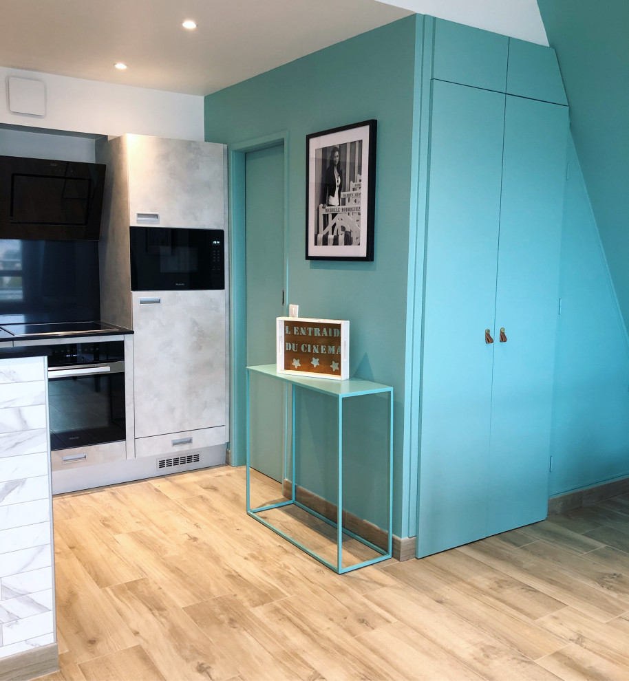 Photo of a small beach style l-shaped open plan kitchen in Le Havre with flat-panel cabinets, grey cabinets, granite benchtops, grey splashback, granite splashback, black appliances, ceramic floors and black benchtop.