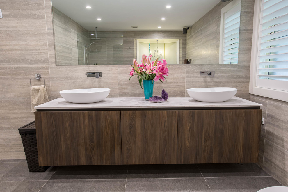 Inspiration for a mid-sized modern master bathroom in Sydney with flat-panel cabinets, dark wood cabinets, a freestanding tub, a curbless shower, a wall-mount toilet, gray tile, ceramic tile, grey walls, ceramic floors, a wall-mount sink, marble benchtops, grey floor and an open shower.
