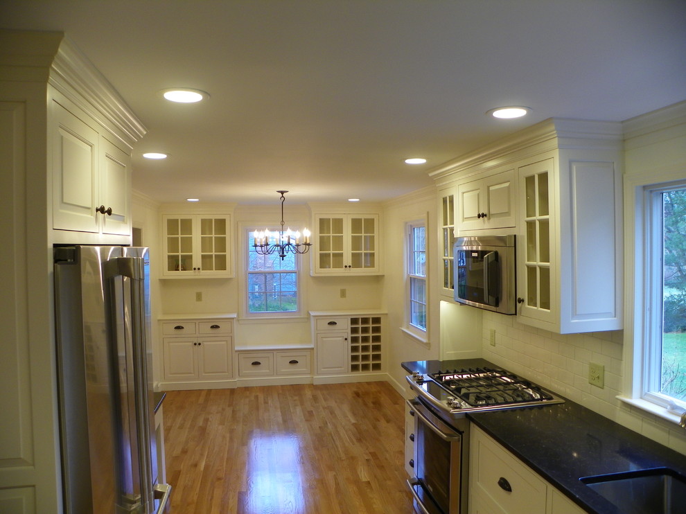 Photo of a mid-sized transitional u-shaped eat-in kitchen in Boston with beaded inset cabinets, white cabinets, no island, an undermount sink, quartz benchtops, white splashback, subway tile splashback, stainless steel appliances and light hardwood floors.