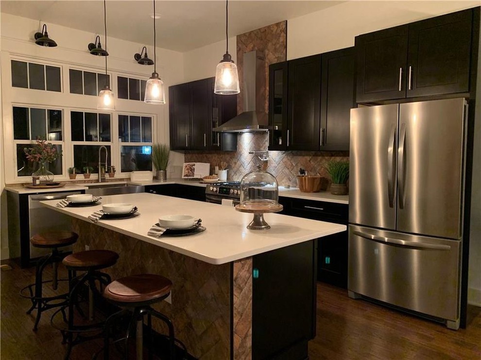 Large country l-shaped eat-in kitchen in Indianapolis with a farmhouse sink, shaker cabinets, dark wood cabinets, quartzite benchtops, brown splashback, brick splashback, stainless steel appliances, dark hardwood floors, with island, brown floor and white benchtop.