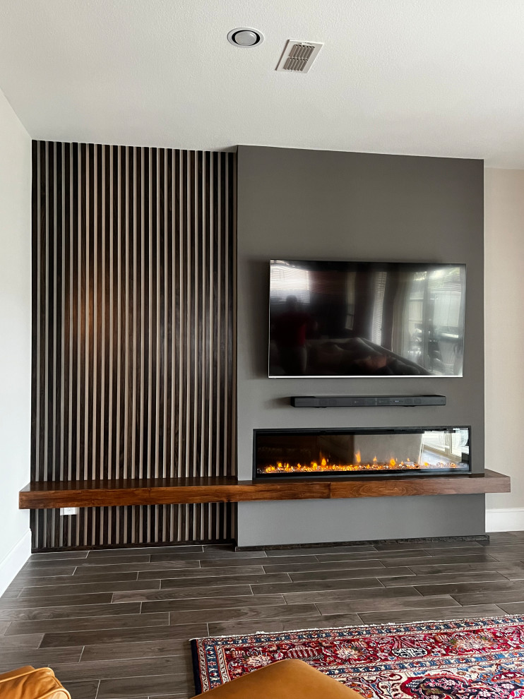 Идея дизайна: изолированная гостиная комната среднего размера в стиле модернизм с с книжными шкафами и полками, серыми стенами, полом из керамической плитки, стандартным камином, фасадом камина из дерева, телевизором на стене и коричневым полом