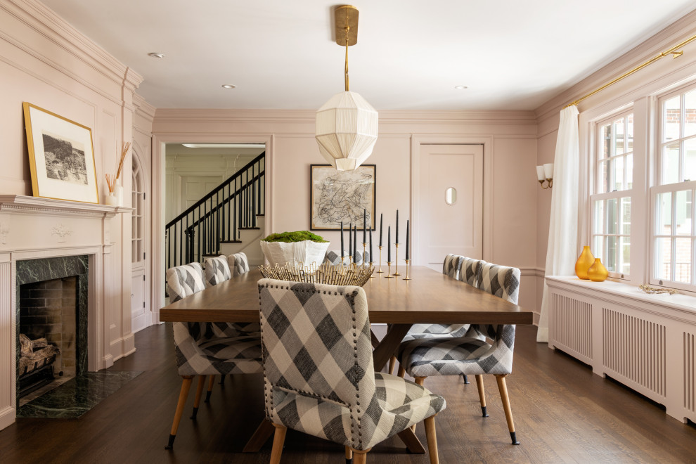 Photo of a transitional separate dining room in New York with pink walls, medium hardwood floors, a standard fireplace, a stone fireplace surround, brown floor and panelled walls.