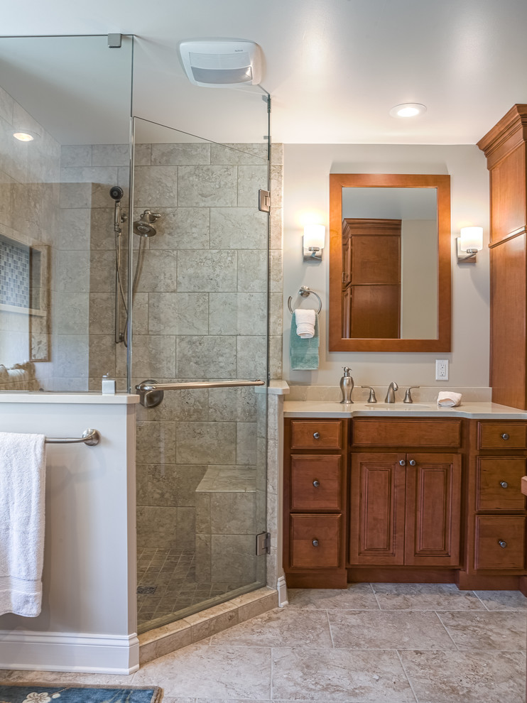 Example of a mid-sized transitional master beige tile and glass tile porcelain tile corner shower design with an undermount sink, raised-panel cabinets, medium tone wood cabinets, quartz countertops, a two-piece toilet and beige walls