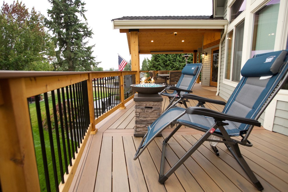 Example of a large mountain style backyard deck design in Seattle with a roof extension and a fire pit