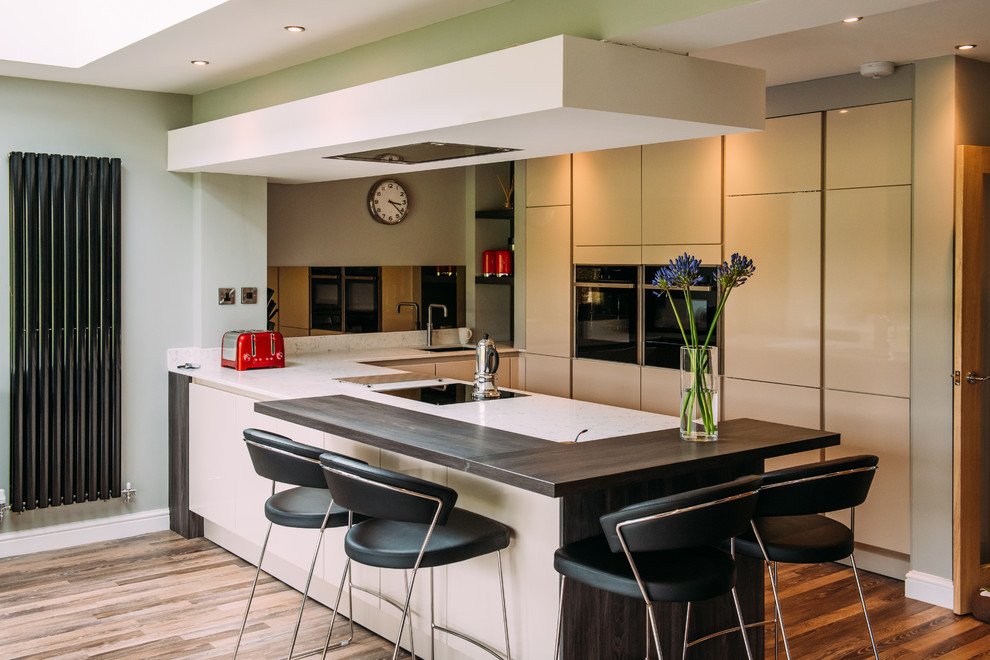 Small contemporary u-shaped eat-in kitchen in Other with mirror splashback, an undermount sink, flat-panel cabinets, white cabinets, limestone benchtops, panelled appliances, medium hardwood floors, a peninsula and brown floor.