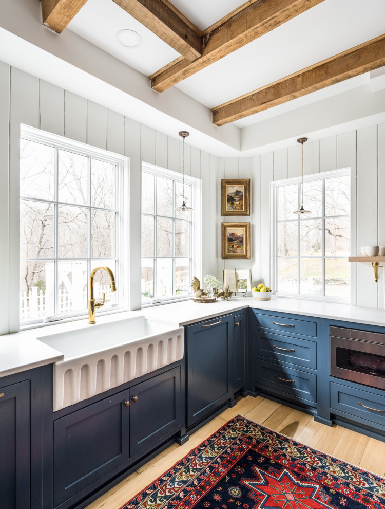 Photo of a mid-sized country u-shaped separate kitchen in Nashville with a farmhouse sink, beaded inset cabinets, blue cabinets, quartz benchtops, white splashback, timber splashback, stainless steel appliances, light hardwood floors, with island, yellow floor and white benchtop.