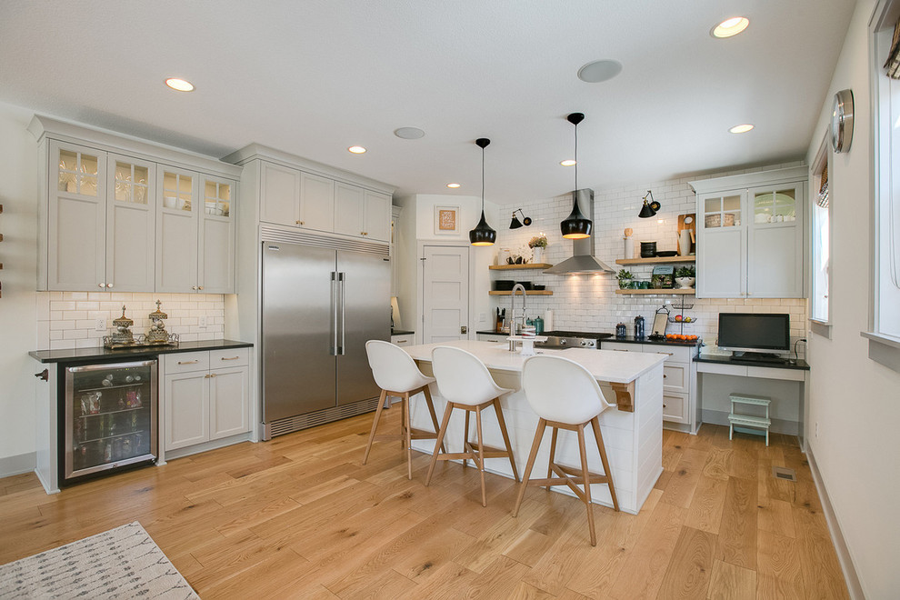 Inspiration for a transitional l-shaped kitchen in Minneapolis with shaker cabinets, white cabinets, white splashback, subway tile splashback, stainless steel appliances, light hardwood floors, with island and brown floor.