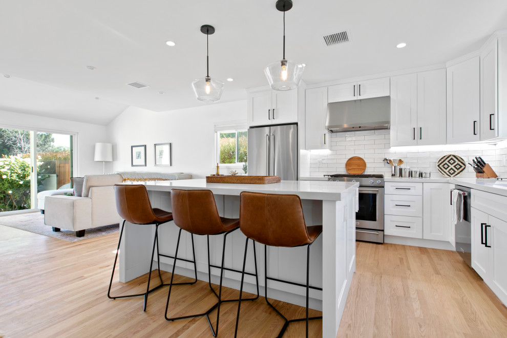 Inspiration for a large transitional eat-in kitchen in Los Angeles with shaker cabinets, white cabinets, quartz benchtops, white splashback, subway tile splashback, stainless steel appliances, light hardwood floors, with island, beige floor and white benchtop.