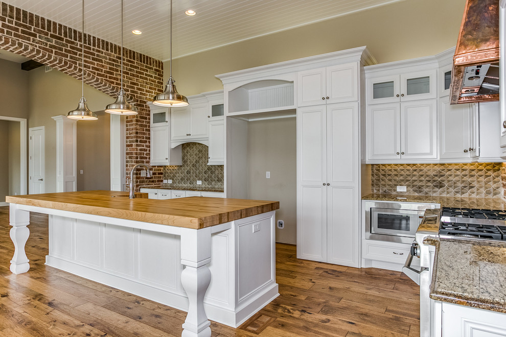 Mid-sized transitional l-shaped eat-in kitchen in Wichita with a farmhouse sink, recessed-panel cabinets, white cabinets, wood benchtops, red splashback, brick splashback, stainless steel appliances, medium hardwood floors, with island and brown floor.