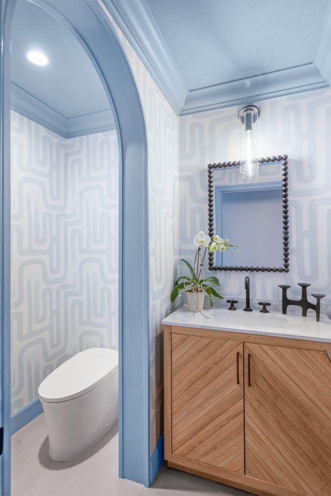 Cette image montre un petit WC et toilettes design en bois brun avec un bidet, un mur bleu, un sol en carrelage de porcelaine, un lavabo posé, un plan de toilette en marbre, un sol gris, un plan de toilette blanc, meuble-lavabo sur pied et du papier peint.