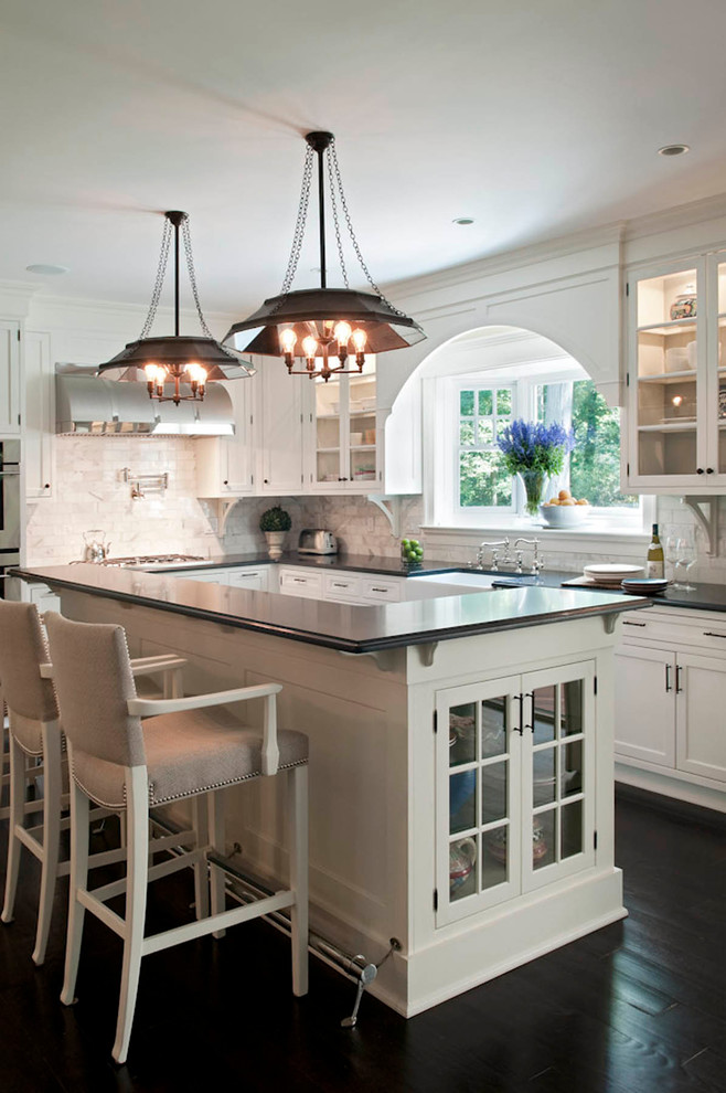 Mid-sized country l-shaped eat-in kitchen in New York with shaker cabinets, white cabinets, solid surface benchtops, white splashback, with island, a farmhouse sink, stone tile splashback, stainless steel appliances and dark hardwood floors.
