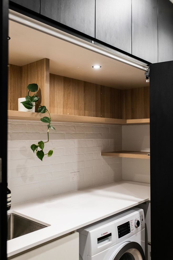 This is an example of a large contemporary galley utility room in Melbourne with porcelain floors, brown floor, a drop-in sink, open cabinets, light wood cabinets, laminate benchtops, white walls, an integrated washer and dryer and white benchtop.