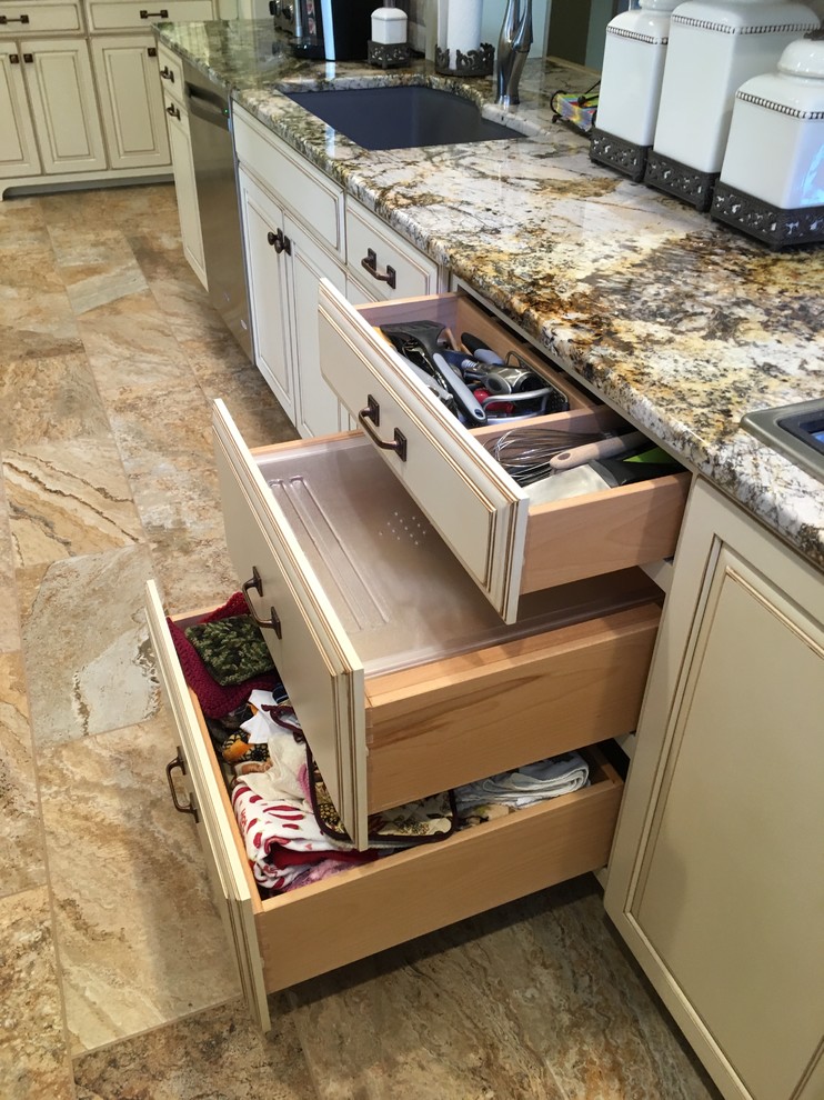 Example of a large transitional galley porcelain tile enclosed kitchen design with an undermount sink, raised-panel cabinets, distressed cabinets, granite countertops, beige backsplash, stone tile backsplash, stainless steel appliances and a peninsula