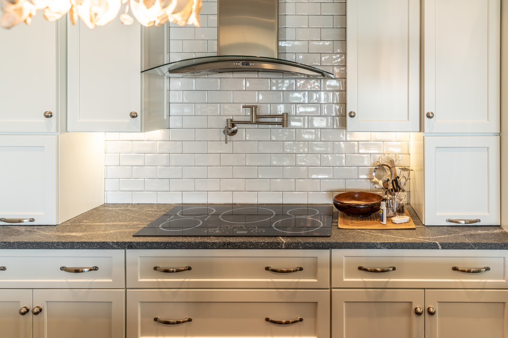 Photo of a mid-sized transitional galley separate kitchen in Charleston with a farmhouse sink, recessed-panel cabinets, white cabinets, granite benchtops, white splashback, ceramic splashback, stainless steel appliances, with island and grey benchtop.