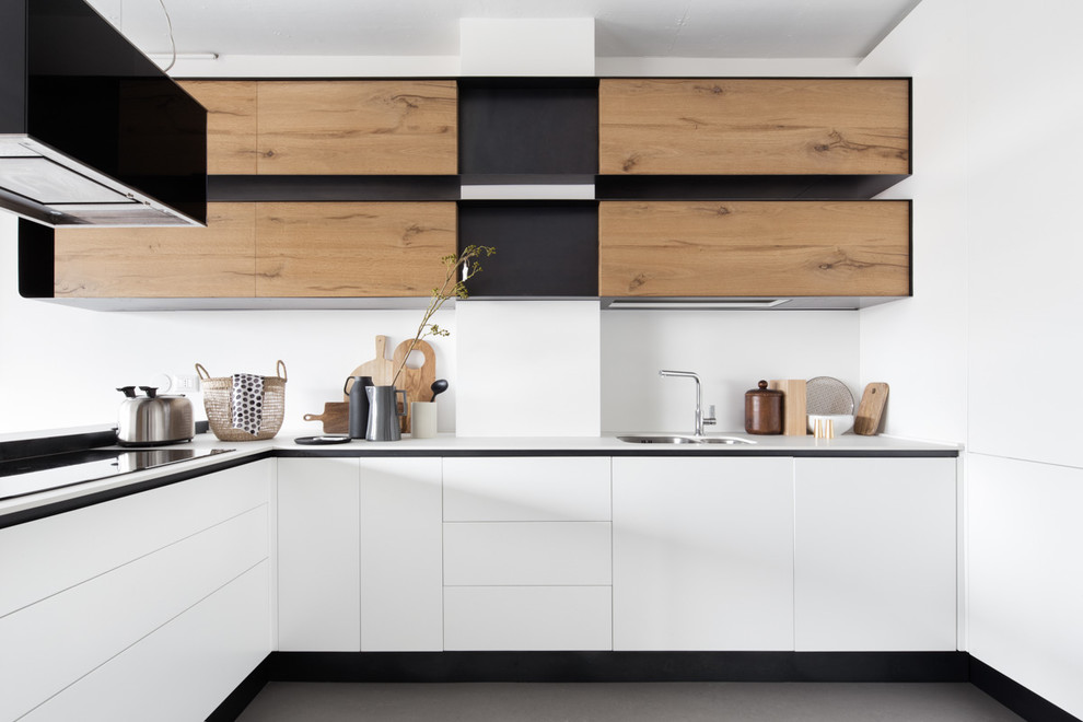 Design ideas for a mid-sized contemporary l-shaped kitchen in Milan with an undermount sink, flat-panel cabinets, white cabinets, white splashback, concrete floors, a peninsula, grey floor and white benchtop.